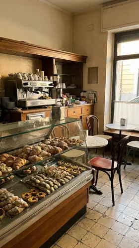 Photo of a pastry shop interior: a display of croissants and pastries, a coffee machine, small tables.